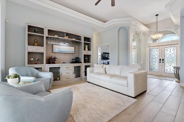 living room with french doors, ceiling fan with notable chandelier, light hardwood / wood-style flooring, and built in shelves