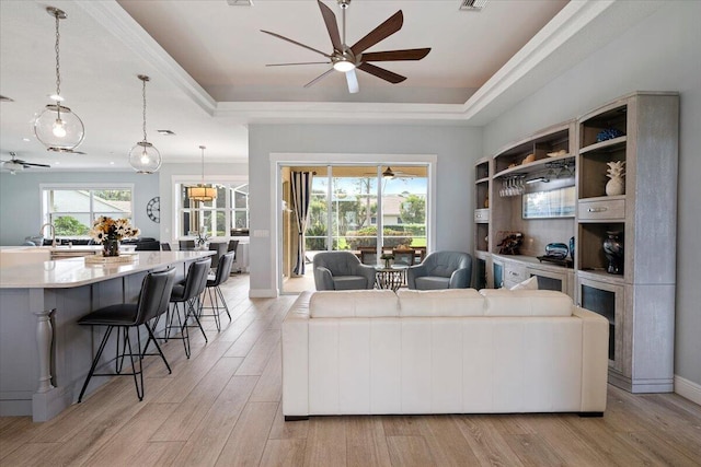 living room with light wood-type flooring, a tray ceiling, and plenty of natural light