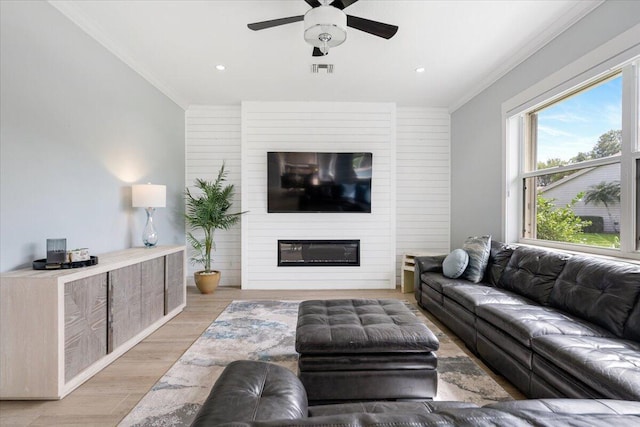 living room featuring ceiling fan, a large fireplace, light hardwood / wood-style flooring, and ornamental molding