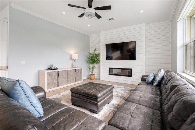 living room with ceiling fan, a fireplace, crown molding, and light hardwood / wood-style flooring