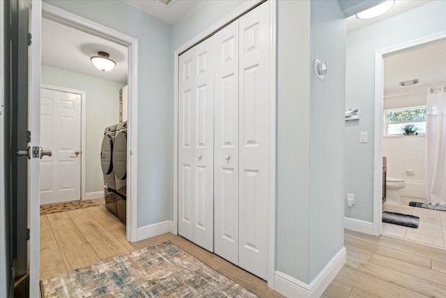 hall featuring a textured ceiling, light wood-type flooring, and washing machine and clothes dryer