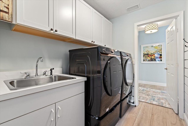 washroom with cabinets, sink, light hardwood / wood-style flooring, washer and dryer, and a textured ceiling