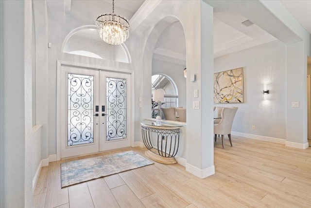 foyer with french doors, an inviting chandelier, light hardwood / wood-style flooring, and crown molding