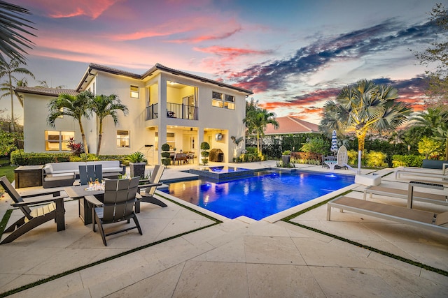 pool at dusk with an in ground hot tub, an outdoor living space, pool water feature, and a patio area