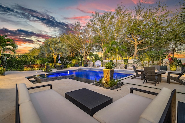 pool at dusk featuring an in ground hot tub and a patio