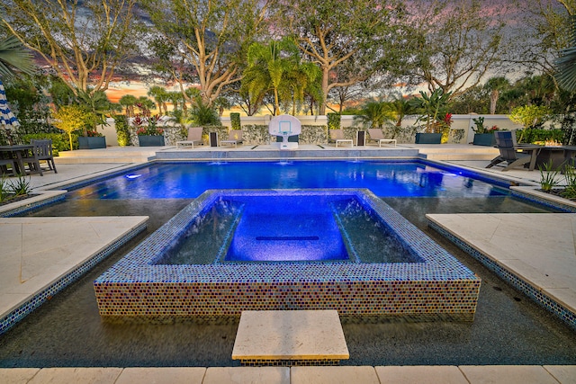 pool at dusk featuring pool water feature, an in ground hot tub, and a patio