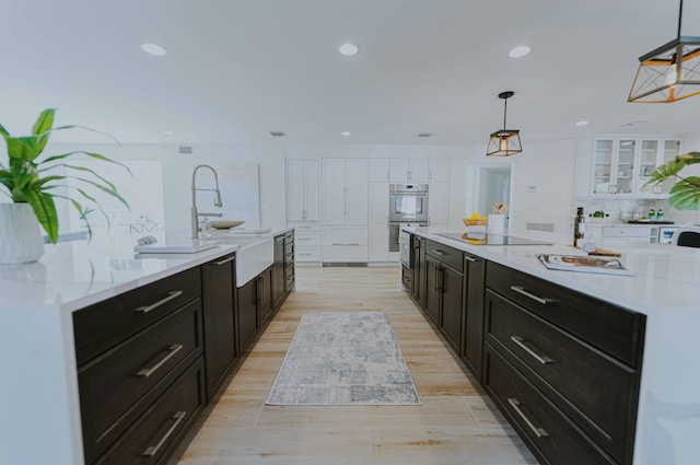 kitchen featuring a spacious island, white cabinets, pendant lighting, and light hardwood / wood-style floors