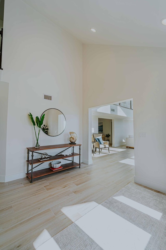 corridor with high vaulted ceiling and light hardwood / wood-style flooring