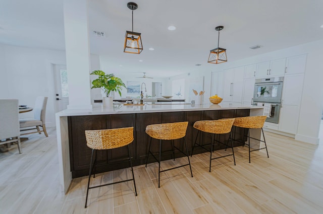 bar with white cabinets, light wood-type flooring, double oven, and hanging light fixtures