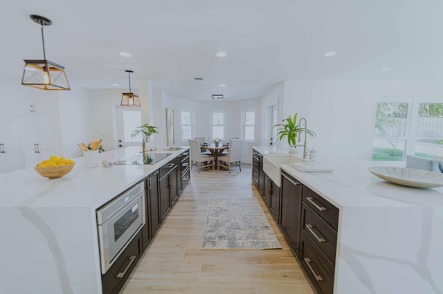 kitchen featuring light stone counters, sink, a large island with sink, decorative light fixtures, and light hardwood / wood-style floors