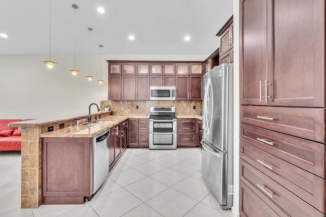 kitchen featuring kitchen peninsula, light stone counters, stainless steel appliances, sink, and decorative light fixtures