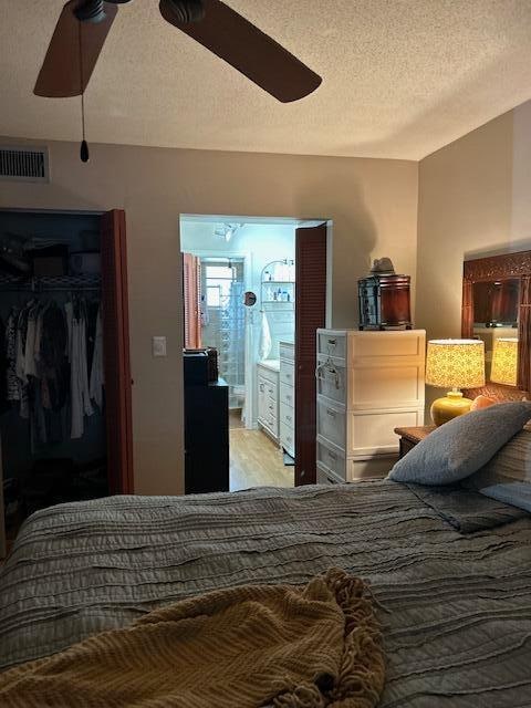 bedroom with light hardwood / wood-style flooring, ceiling fan, a textured ceiling, connected bathroom, and a closet