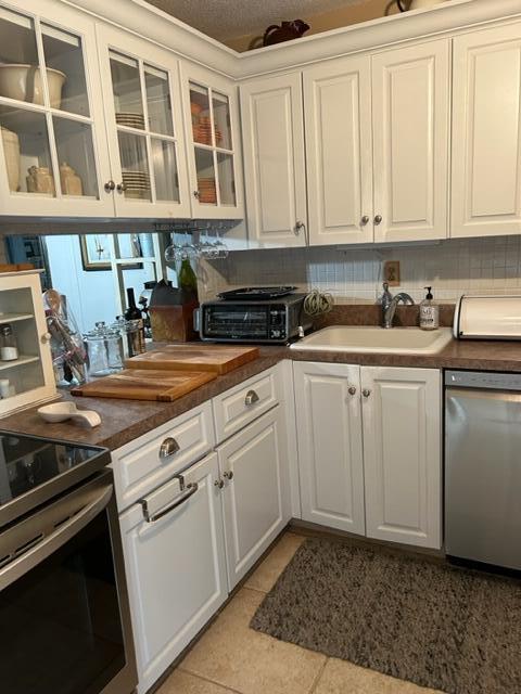 kitchen featuring backsplash, sink, light tile patterned flooring, white cabinetry, and stainless steel appliances