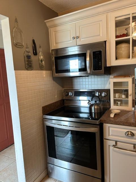 kitchen featuring white cabinets, a textured ceiling, light tile patterned floors, tile walls, and appliances with stainless steel finishes