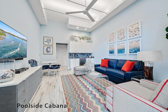 living room with a high ceiling, light wood-type flooring, and ceiling fan