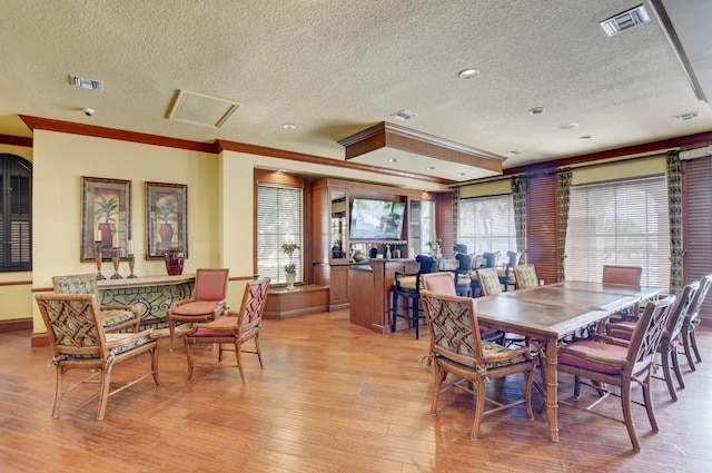 dining space featuring a textured ceiling, light wood-type flooring, and crown molding