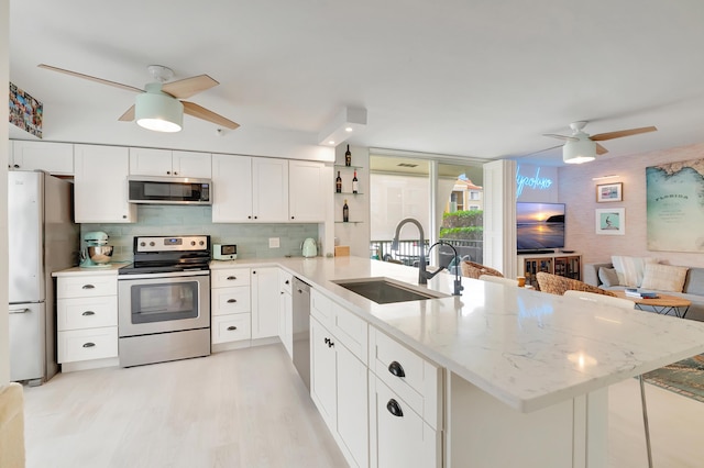 kitchen featuring sink, light stone counters, kitchen peninsula, white cabinets, and appliances with stainless steel finishes