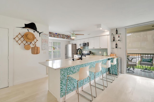 kitchen featuring kitchen peninsula, appliances with stainless steel finishes, backsplash, white cabinetry, and a breakfast bar area