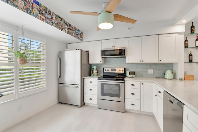 kitchen with appliances with stainless steel finishes, backsplash, light stone counters, ceiling fan, and white cabinets