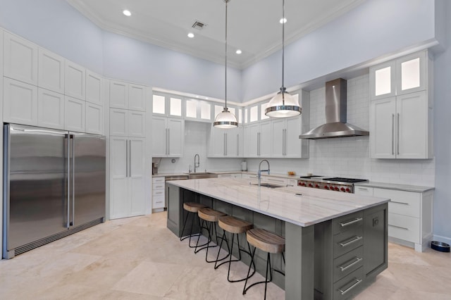 kitchen with white cabinetry, high end fridge, wall chimney exhaust hood, and a kitchen island with sink