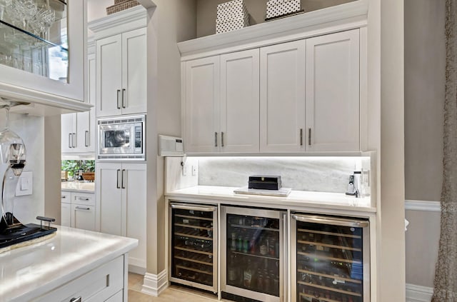 bar featuring white cabinets, stainless steel microwave, and beverage cooler