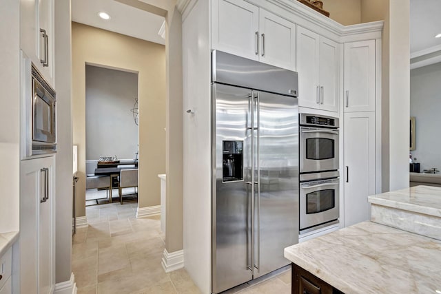 kitchen featuring built in appliances, white cabinets, light tile patterned floors, and light stone counters