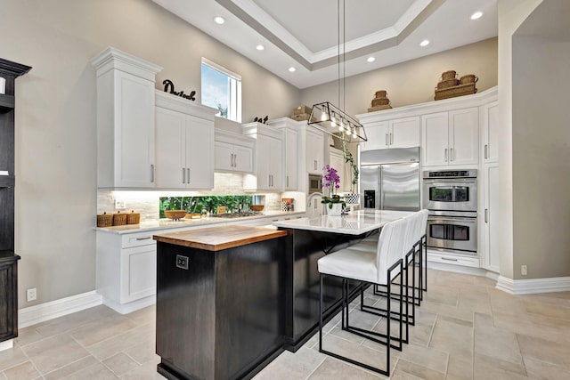 kitchen featuring appliances with stainless steel finishes, backsplash, decorative light fixtures, a center island with sink, and white cabinets