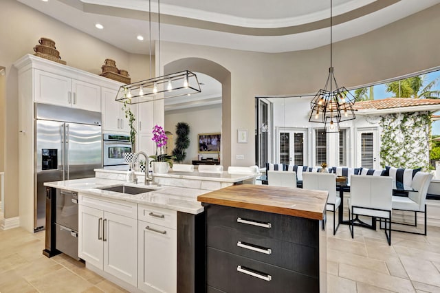 kitchen featuring a kitchen island with sink, white cabinets, sink, appliances with stainless steel finishes, and decorative light fixtures