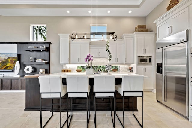 kitchen with white cabinets, built in appliances, plenty of natural light, and a kitchen island with sink