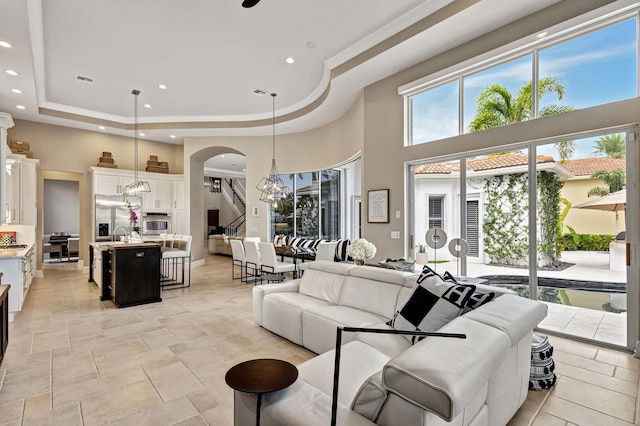 living room featuring a tray ceiling, sink, a towering ceiling, and a chandelier