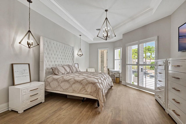 bedroom featuring a raised ceiling, light wood-type flooring, crown molding, and an inviting chandelier