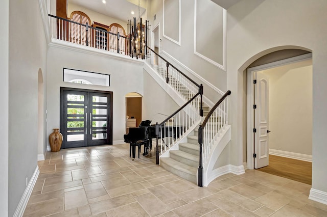 foyer featuring a chandelier, a towering ceiling, light hardwood / wood-style flooring, and french doors