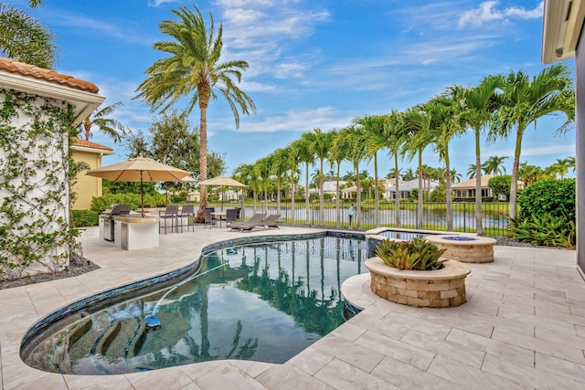 view of pool with grilling area, a water view, a patio, and an outdoor kitchen