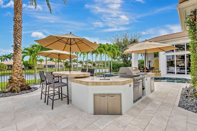 view of patio / terrace featuring an outdoor kitchen, a water view, and a bar