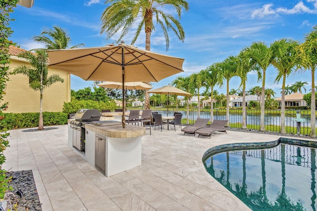 view of swimming pool featuring an outdoor kitchen, a water view, a patio area, area for grilling, and a bar