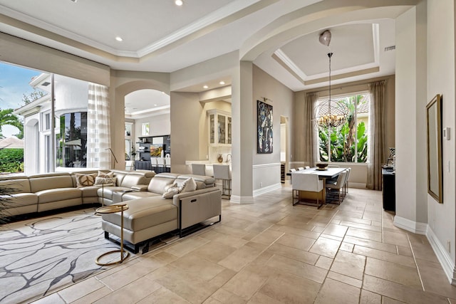 living room with a raised ceiling, ornamental molding, and a chandelier