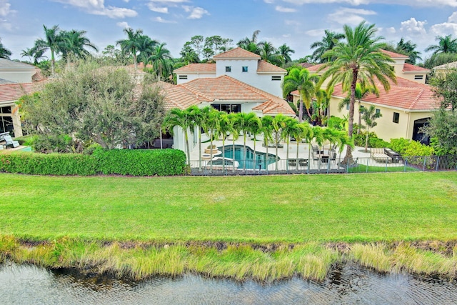 rear view of house with a lawn, a water view, and a fenced in pool