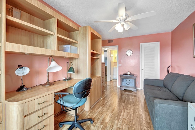 office featuring a textured ceiling, light wood-type flooring, ceiling fan, and built in desk