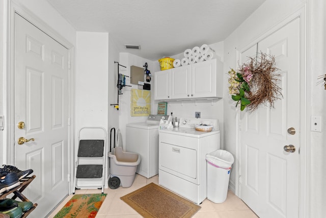 washroom with cabinets, independent washer and dryer, a textured ceiling, and light tile patterned floors