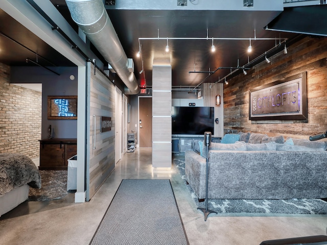 living room featuring wood walls, rail lighting, concrete flooring, and brick wall