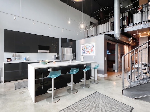 kitchen with stainless steel fridge, sink, a kitchen island with sink, and a high ceiling