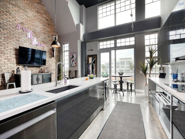 kitchen with a high ceiling, hanging light fixtures, sink, appliances with stainless steel finishes, and brick wall