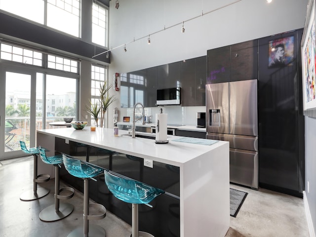 kitchen featuring a high ceiling, a center island with sink, a kitchen breakfast bar, sink, and stainless steel fridge with ice dispenser