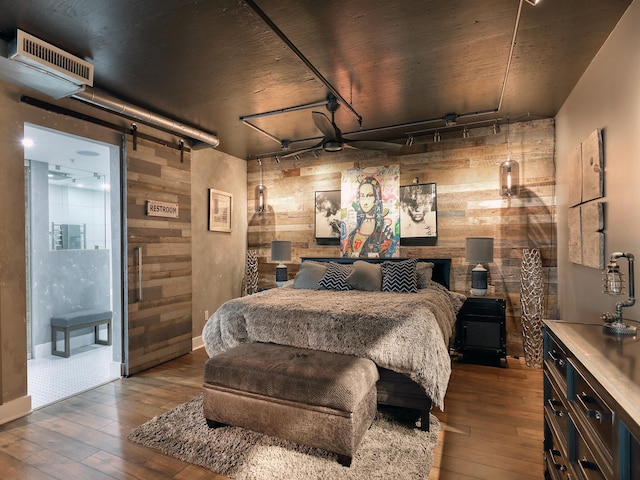 bedroom featuring a barn door, wooden walls, wood-type flooring, and track lighting