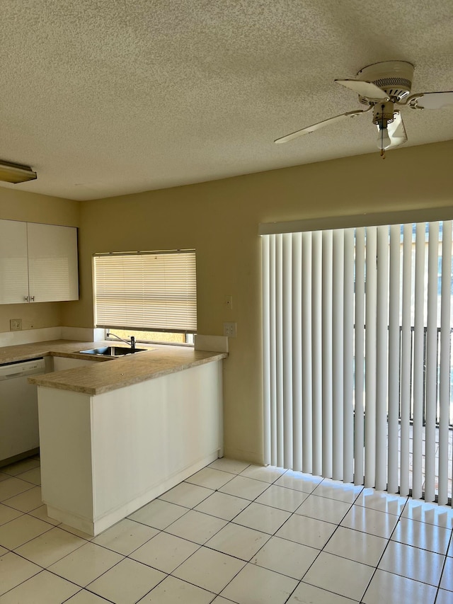 kitchen featuring dishwasher, sink, light tile patterned flooring, kitchen peninsula, and white cabinets