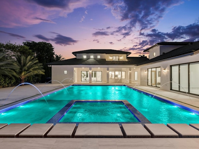 pool at dusk with a patio and a pool with connected hot tub