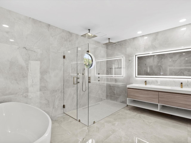 full bath featuring vanity, a marble finish shower, a freestanding tub, recessed lighting, and tile walls