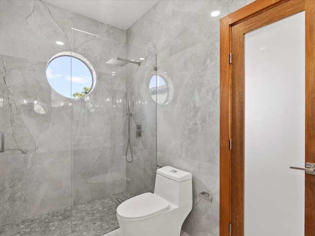 full bath with a marble finish shower, toilet, and tile walls