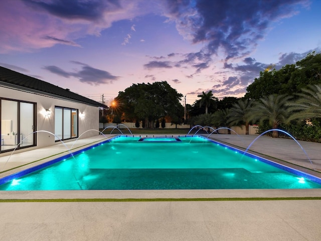 pool at dusk with an outdoor pool and a patio area