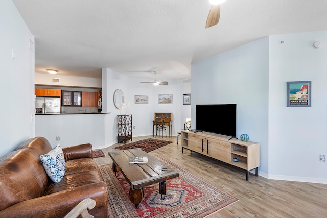 living room with ceiling fan, light hardwood / wood-style floors, and a textured ceiling